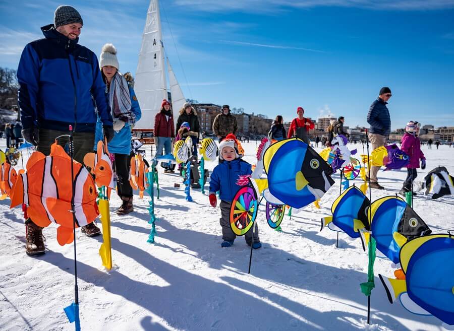 Child explores the small kites on frozen Lake Mendota with the legendary Mary B. Ice Boat in the background